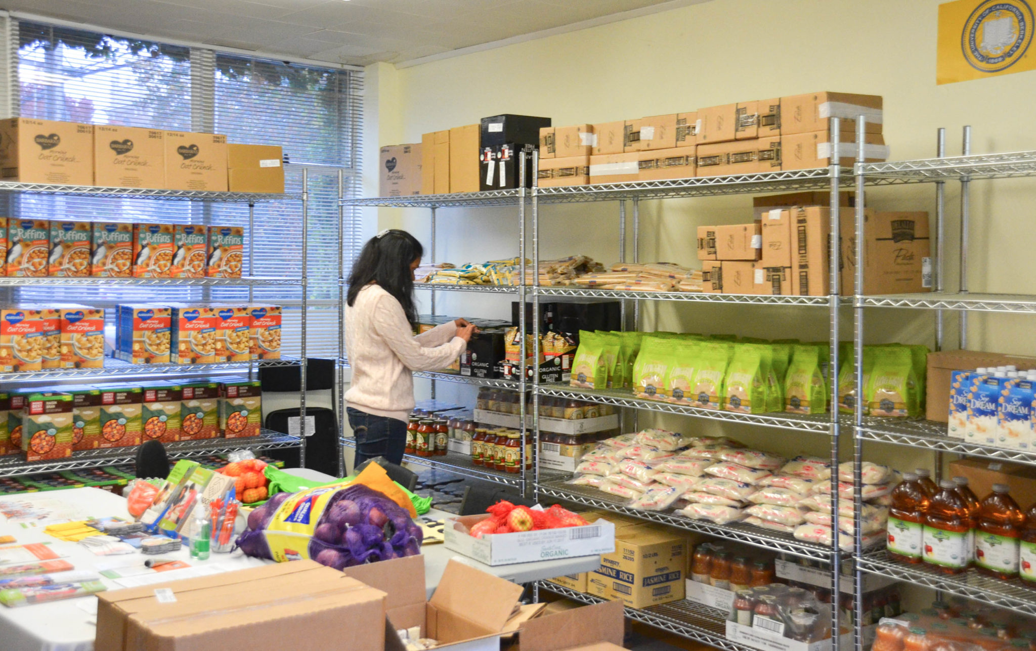 Student shops at the UC Berkeley Food Pantry, reaching towards some food items on a rack.