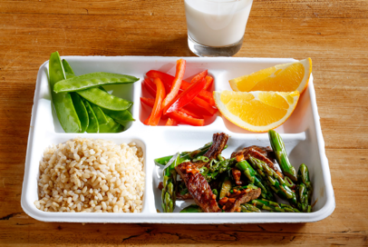 Healthful school lunch: snap peas, bell pepper strips, orange, brown rice, asparagus and other mixed veggies.