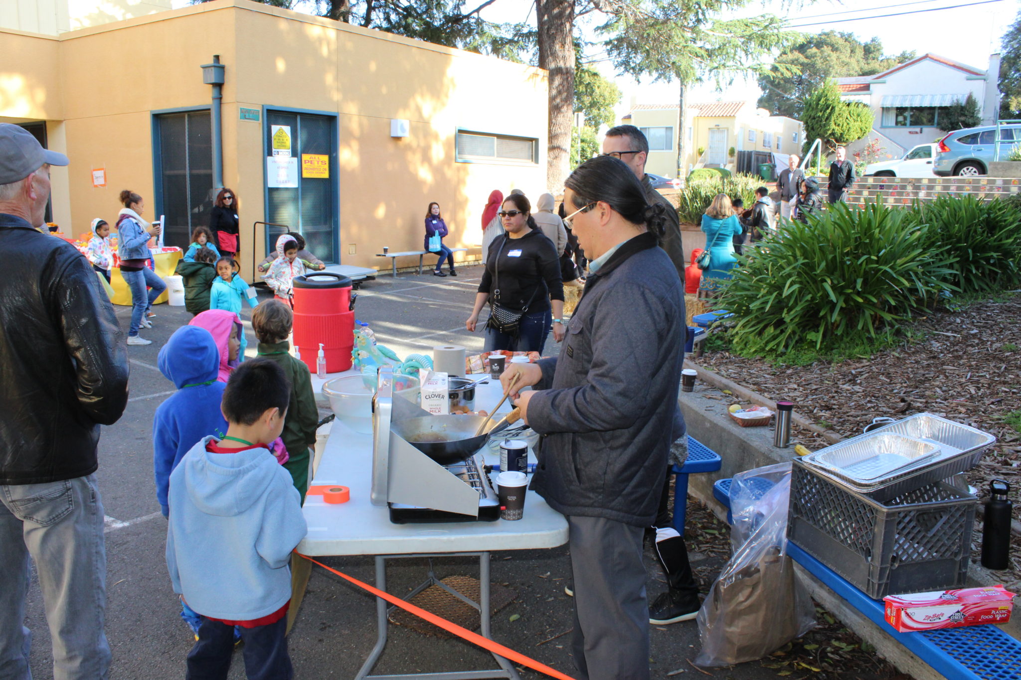 A volunteer cooks food in a pan while kids watch.