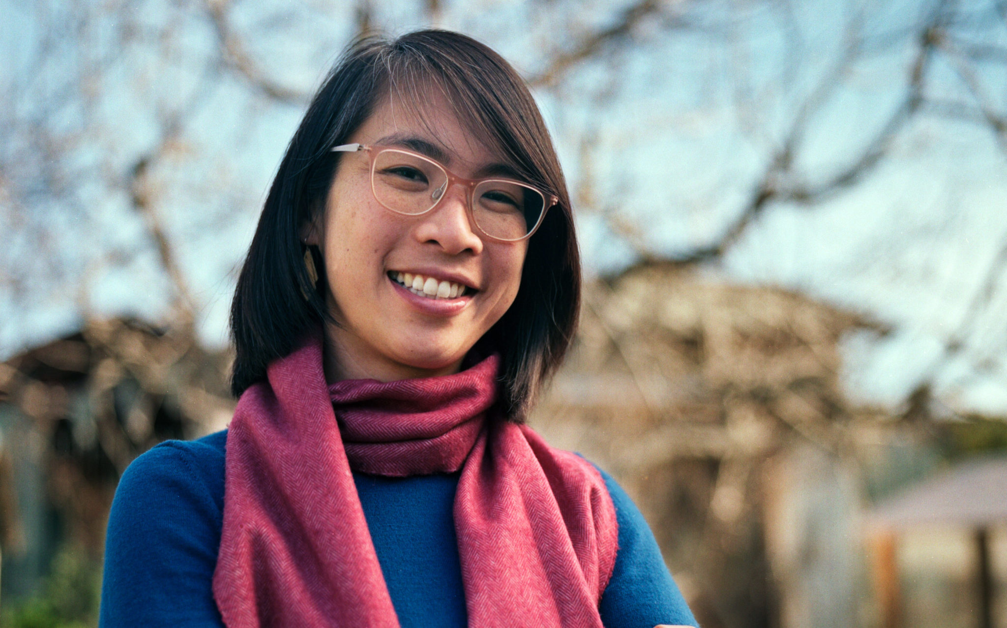 photo of Mai Nguyen standing in blue sweater with red scarf. photo by Fabian Aguirre